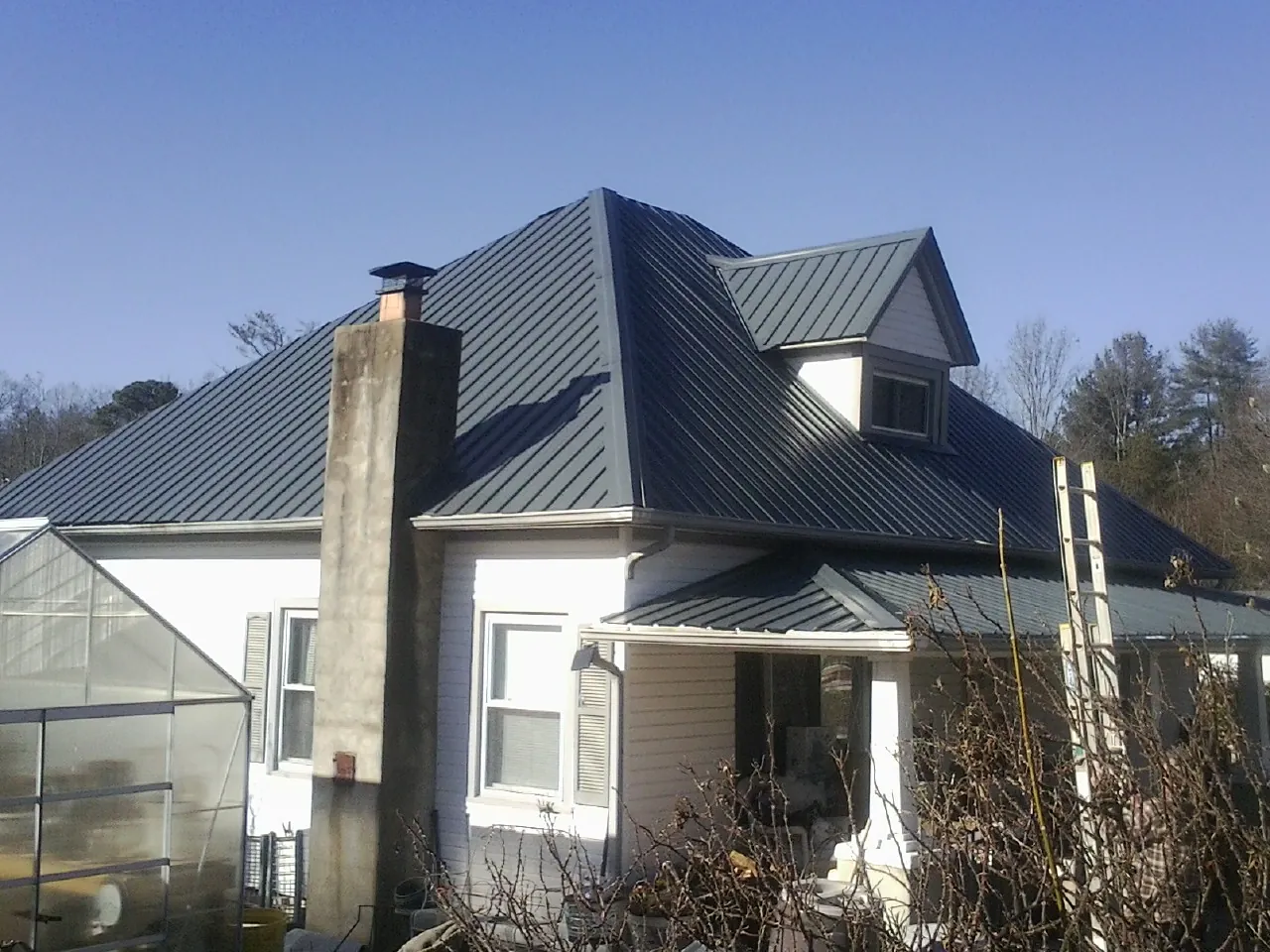 Dark blue standing seam metal roof on a white farmhouse with dormer — Slate & Tile Roof Repair by Roofing Brothers in Quinlan
