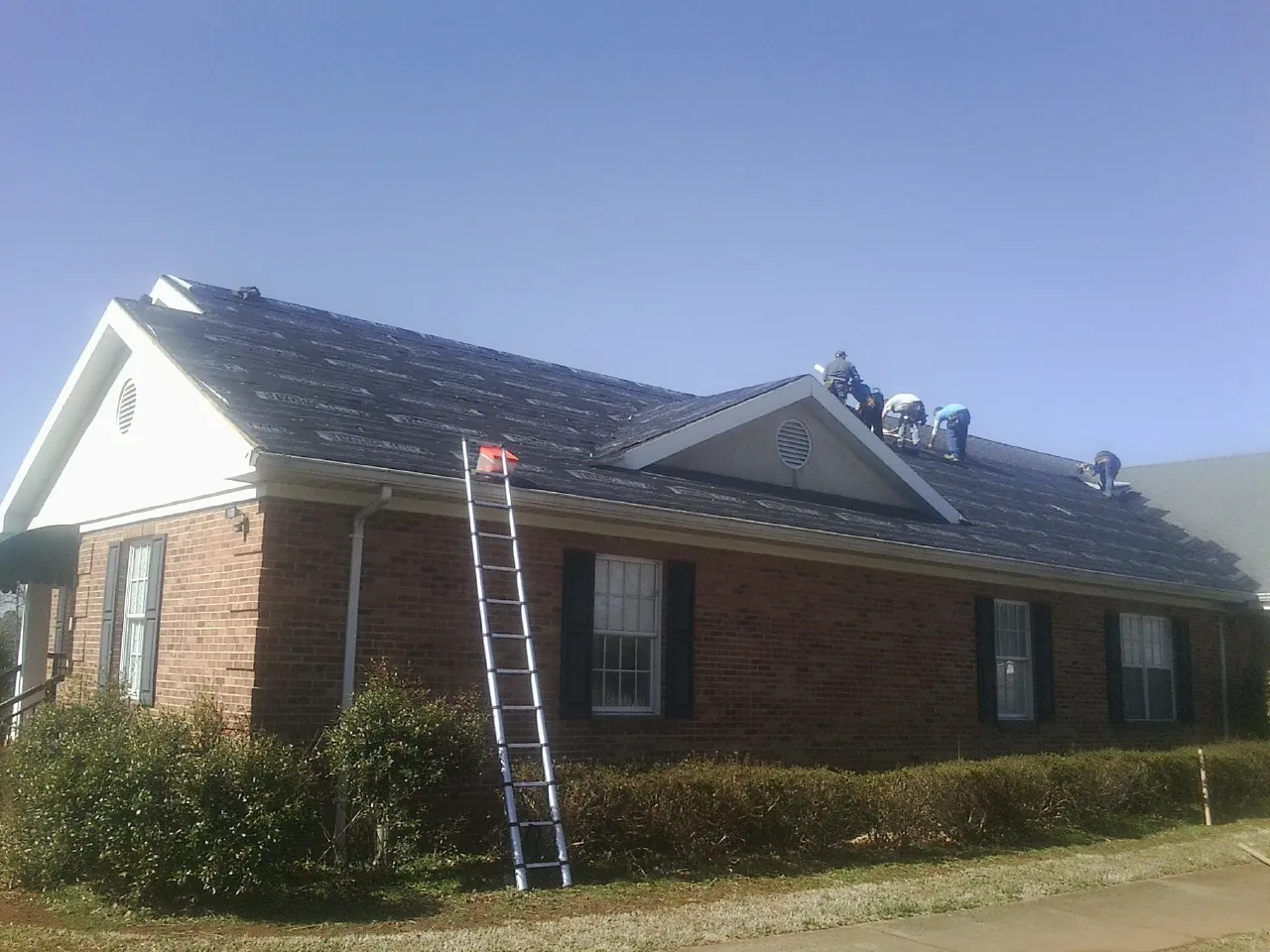 Crew tearing shingles off a brick ranch roof with a ladder set — Metal Roof Repair work by our crew in Quinlan