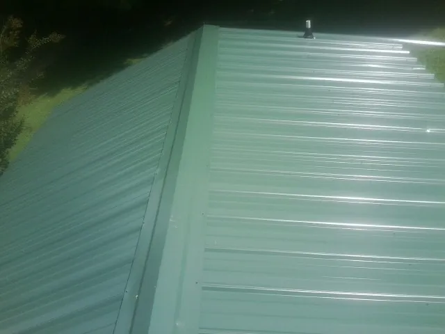 New green metal panels meeting at the ridge of a roof — Flat Roof Repair work by our crew in Quinlan