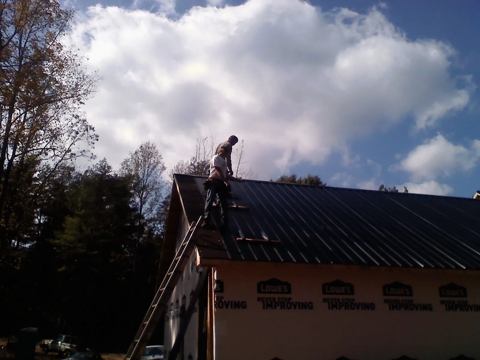 Roofer fastening dark metal panels high against a cloudy sky, from a Roof Inspection job in Quinlan