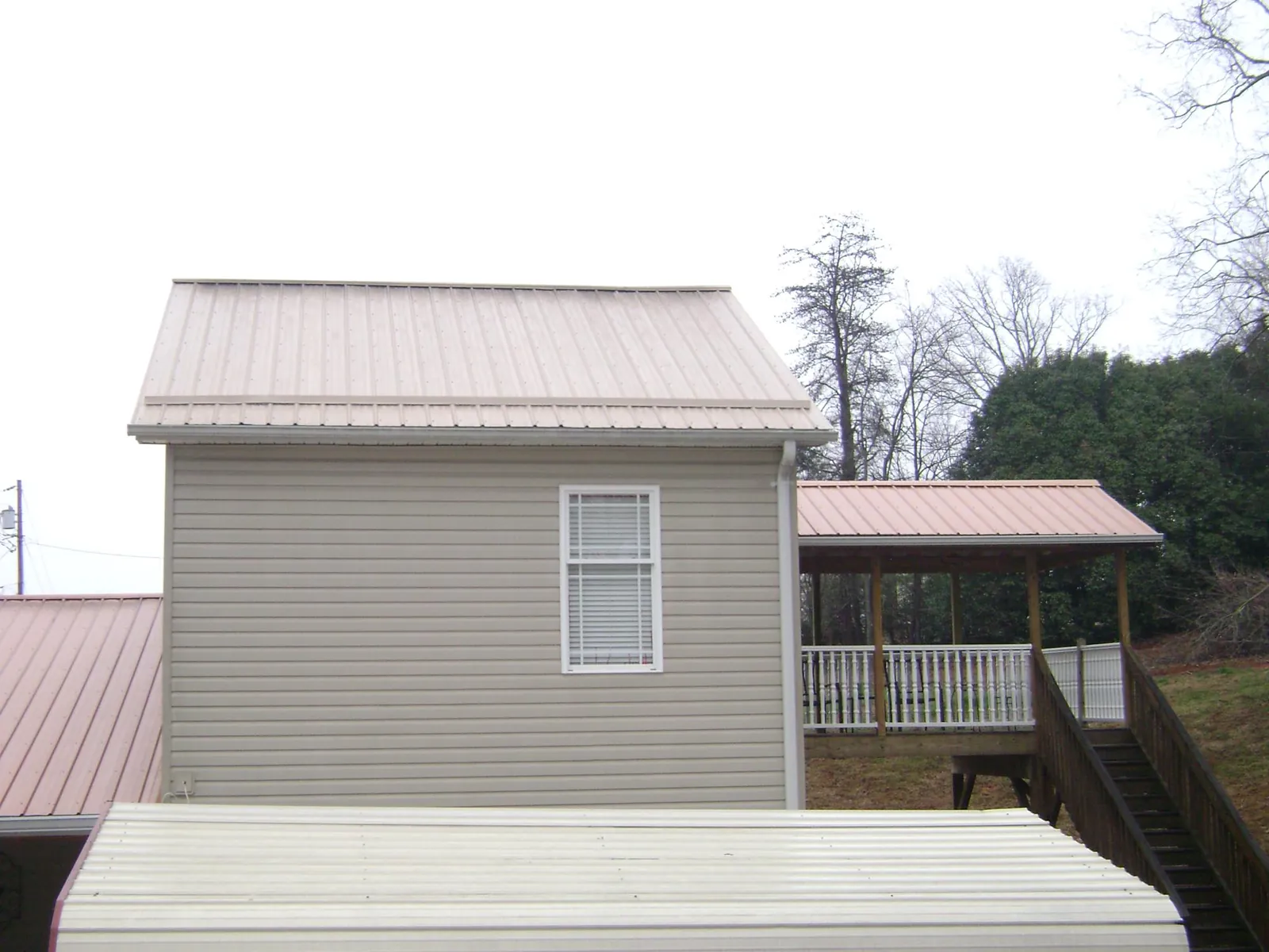 Tan metal roofs on a two story addition and attached porch, from a Roof Replacement job in Quinlan